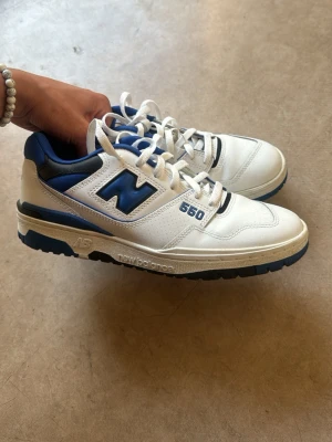 New Balance sneakers - Snygga New Balance 650 sneakers i vitt och blått med klassisk logga på sidan. Skorna har lågt skaft, robust sula och detaljer i läder och textil. Perfekta för dig som gillar retrostil och sportig vibe.