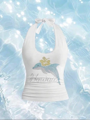 Vit halterneck linnetopp med delfin - Snygg vit halterneck linnetopp med knyt i nacken. Framsidan har en blå delfin med gul blomma och texten 'Hawaii' i glittriga stenar. Perfekt för sommarens alla äventyr.