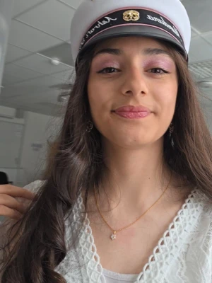 Studentmössa med rosa tunn band och guld kokard - Säljer en klassisk studentmössa i vitt med tunn rosa band och guldfärgad kokard framtill. Mössan har broderad text och dekorativ detalj i guld. Perfekt accessoar till studenten för en snygg och traditionell look.