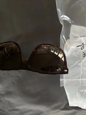 Bruna  solglasögon Ray-Ban - Svarta solglasögon från Ray-Ban med  båge och mörka glas. Klassisk och trendig look med diskret Ray-Ban-logga på linsen. Perfekta för att höja din stil till nästa nivå. Helt oanvänd 