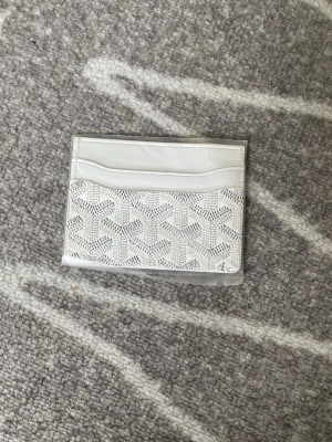 Vit kortfodral  - Snyggt vitt kortfodral från med det klassiska mönstret framtill. Fodralet har flera kortfack och är gjort i läder med detaljer i canvas. Perfekt för dig som vill ha en stilren och exklusiv accessoar i fickan.