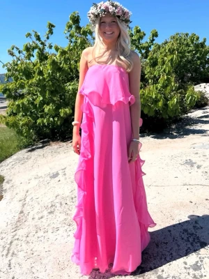 Rosa långklänning med volanger - Säljer en superfin rosa långklänning med volangdetaljer och axelbandslös design. Klänningen har ett luftigt fall och passar perfekt till sommarens alla tillfällen. Materialet känns lätt och svalt, och färgen är riktigt härlig. Använt en gång, skriv för fler bilder.
