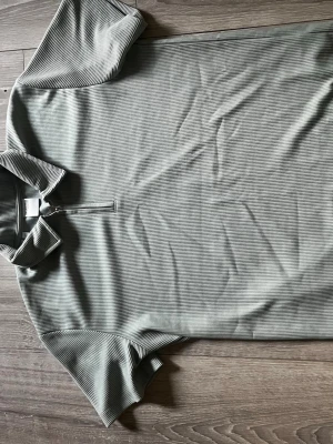 Randig polotopp från Selected Homme - Snygg polotopp från Selected Homme i diskret ljusgrått med tunna ränder. Tröjan har krage, kort ärm och dragkedja framtill. Perfekt för en stilren och avslappnad look.