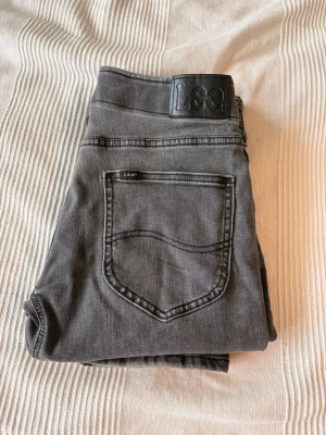 Grå jeans från Lee raka ben - Snygga grå jeans från Lee med raka ben och klassisk femficksmodell. Jeansen har svart Lee-lapp bak i midjan och är tillverkade i mjukt denimtyg. Perfekta för en avslappnad och stilren look. W 29 L 32