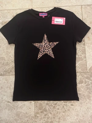 Svart t-shirt med leopardstjärna - Svart t-shirt från Edikted med en stor stjärna i leopardmönster på bröstet. Klassisk passform och rund halsringning. Tillverkad i mjuk bomull som känns skön mot huden. 