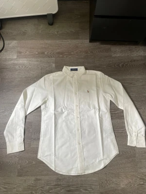 Vit skjorta från Polo Ralph Lauren - Klassisk vit skjorta från Polo Ralph Lauren med broderad logga på bröstet. Perfekt till både jeans och chinos för en clean och stilren look. Storlek L men skulle säga att den sitter som en M/S.