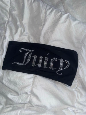 Svart Juicy Couture topp med diamanter - Cool svart bandeau tubtopp från Juicy Couture med glittriga stenar som bildar texten 'Juicy' på framsidan. Perfekt för att skapa en trendig look och funkar till många olika outfits. Materialet är mjukt och stretchigt för en bekväm passform.