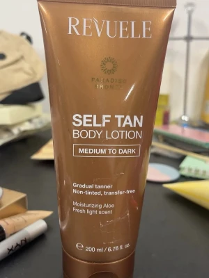Self Tan Body Lotion  - Brun-utan-sol lotion från Revolution i nyansen Medium to Dark. Ger gradvis solbrun färg, är oparfymerad och kladdfri. Innehåller återfuktande aloe vera och har en fräsch, lätt doft. Tuben rymmer 200 ml och har en snygg bronsfärgad design. Rosett kan tas bort😅tyckte bara de var lite sött✨helt oanvänd!!! Hoppas de går att se! Helt NY! 👀🎉brun utan sol är dyrt, men jag säljer billigare😀för jag vet att jag själv gillar det🤪