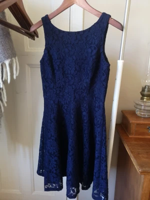 Mörkblå spetsklänning ärmlös - Snygg mörkblå klänning med spetsdetaljer och ärmlös design. Klänningen har en lätt utställd kjol som ger en feminin siluett. Perfekt för dig som vill ha en elegant look med fina detaljer. Är inte genomskinligt då den har en inbyggd underskjol (se bild 5). Säljes pga garderobs rensning. 