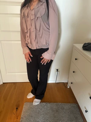 Ljuslila blus med volanger - Trendig ljuslila blus med långa ärmar och snygga volangdetaljer framtill. Blusen har en avslappnad passform och mjukt, tunt tyg som ger ett elegant intryck. Perfekt att styla med både jeans och kostymbyxor.