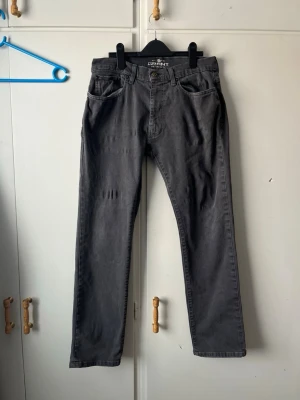 Mörkgrå raka jeans från Gant - Snygga mörkgrå jeans från Gant med rak passform och klassisk femficksdesign. Jeansen har diskreta slitningar på låret och är tillverkade i ett mjukt bomullsmaterial som ger en skön känsla. Perfekta för en avslappnad och stilren look.