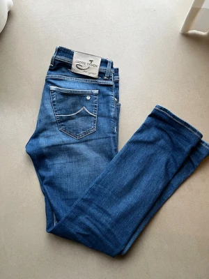 Jacob Cohen jeans - Snygga blå jeans från Jacob Cohen med klassisk femficksdesign och detaljerade sömmar. Jeansen har en patch med logga bak och unika detaljer vid gylfen. Tillverkade i stretchig denim för skön passform. Perfekta för dig som gillar stilrena och exklusiva jeans.