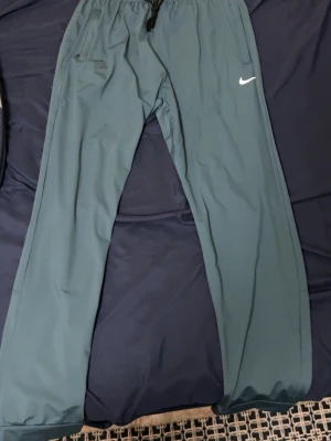 Nike träningsbyxor herr - Snygga träningsbyxor från Nike med vit logga på låret och reflekterande detaljer längs benen. Byxorna har dragsko i midjan och är tillverkade i ett lätt och smidigt material, perfekt för träning eller chill. Klassisk rak passform.