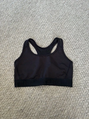 Svart sport-bh med bred resår - En svart sport-bh från STRNG med bred resår och racerback-design. Bh:n är tillverkad i ett stretchigt material som ger bra stöd och komfort. Perfekt för träning och aktiva dagar.