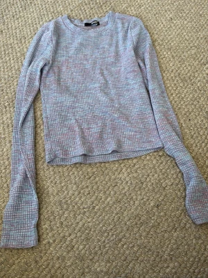 Rutig långärmad topp från BikBok - Säljer en långärmad topp från BikBok med rutigt mönster i ljusa pastellfärger som rosa, blå och lila. Toppen har en rund halsringning och är ribbad för en snygg struktur. Perfekt att matcha med jeans eller kjol.