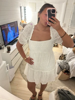 Vit broderad kort klänning med puffärm - Superfin vit kort klänning med broderade blommor och puffärmar. Klänningen har fyrkantig urringning och volang nertill, vilket ger en söt och trendig look. Perfekt för varma dagar och somriga tillfällen. Passar super dra nu när det är dags för stundentklänninh!