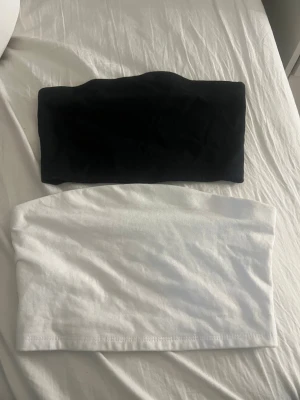 Svart och vit tubtopp i bomull - Två stilrena bandeau tubtoppar i svart och vitt. Båda är ärmlösa och gjorda i mjuk bomull, perfekta att matcha med jeans eller kjol. Enkel och clean design utan detaljer, passar till många olika looks. Väldigt korta