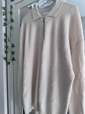 Ziptröja - Snygg beige ziptröja från Jack & Jones med krage och diskret ribbad struktur. Tröjan har dragkedja framtill och är tillverkad i mjukt material som känns skönt mot huden. Perfekt att slänga på sig över en t-shirt.