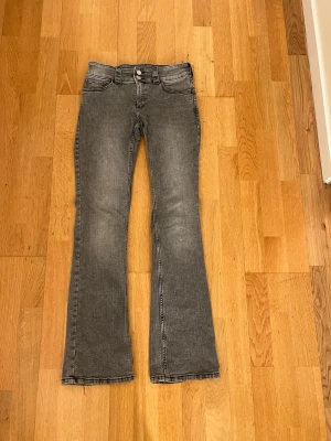 Grå bootcut jeans med låg midja - Säljer ett par grå bootcut jeans med låg midja och klassiska fem fickor. Jeansen har en lätt tvättad look och utsvängda ben.