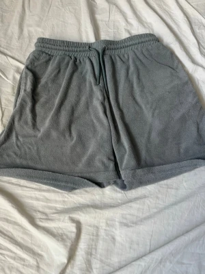 Grå frottéshorts med snörning - Mysiga grå shorts i mjuk frotté med elastisk midja och snörning framtill. Perfekta för lata dagar eller sommarens varma väder. Avslappnad passform och enkel design gör dem till ett måste i garderoben.