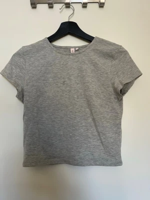 Grå basic topp från Nelly - En enkel och stilren grå topp från Nelly i mjuk bomull. Modellen är kortärmad med rund halsringning. Storlek S köpt på Nelly