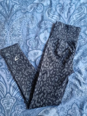 Leopardmönstrade leggings Gymshark - Snygga leggings från Gymshark med leopardmönster och hög midja. Stretchigt material som sitter skönt och formar sig efter kroppen. Perfekta för träning eller chill. Gymshark-logga på benet och vid midjan.