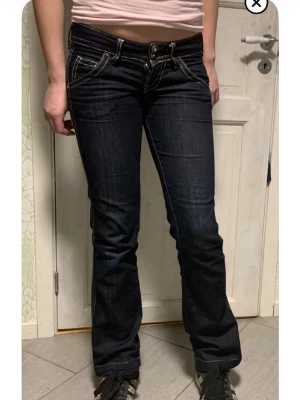 Guess Mörkblå bootcut jeans - Jag säljer ett par lågmidjade mörkblå bootcut jeans som är äkta Guess i storlek 27 i jeans storlek så passar någon dom har storlek 34-36. Från gylf till skrev är det 15 cm så de är väldigt lågmidjade. Innerbenslängden är 76 cm. Mycket bra skick. Jag... se mer