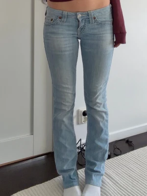 Ljusblå bootcut jeans True Religion - Snygga ljusblå bootcut jeans från True Religion med klassiska kontrastsömmar och broderade bakfickor. Jeansen har låg midja och fem fickor. Perfekta för en avslappnad och trendig look. 