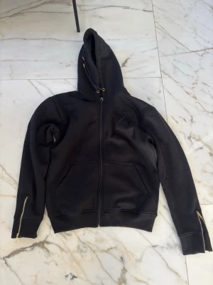 Virelle Hoodie - Hoodie från märket Virelle, helt ny, storlek S, passar även M. Rkt fet med guld detaljer och zip på armarna. 