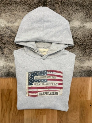 Ljusgrå Denim&supply Ralph Lauren Hoodie - Storlek M - Hej! 👋 Säljer en riktigt snygg hoodie från Denim & Supply – Ralph Laurens ikoniska vintage-subbrand som slutade tillverkas för några år sedan. Den har en unik karaktär och är ett måste för samlare av RL-archive! 🐎 Tröjan är i mycket gott skick för sin ålder, men jag vill vara helt transparent med att det finns ett litet märke på ena ärmen samt en lätt missfärgning på huvan (se närbilder). Det är inget som stör helhetsintrycket när den bärs, men priset är satt därefter. ✨100% äkta med tvättlappar