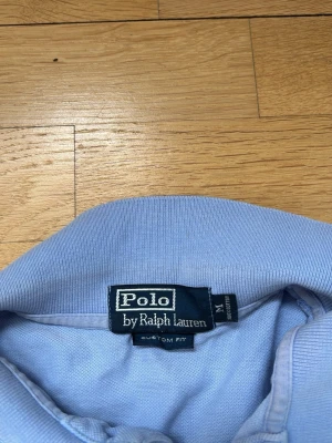 Ljusblå skjorta från Polo Ralph Lauren - Snygg ljusblå skjorta från Polo Ralph Lauren med klassisk krage och broderad logga i limegrönt på bröstet. Skjortan har en custom fit och är perfekt för dig som gillar stilrena plagg med ikonisk design.