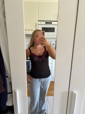 Svart spetslinne med lila detaljer  - Svart spetslinne med lila detaljer. Justerbara band. Märket Miriale. Storlek S skulle jag säga. Inte använd av mig men köpt second hand. 