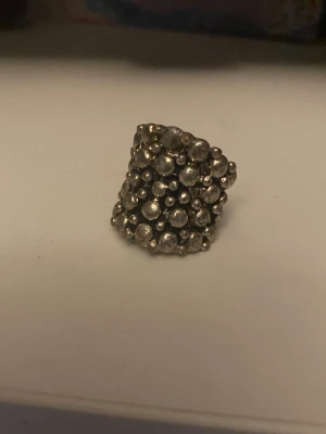 Statementring med bubblig design - Cool statementring i silverfärgad metall med bubblig, texturerad yta. Ringen har en bred form och är täckt av små runda kulor som ger en unik och trendig look. Perfekt accessoar för att lyfta din outfit.