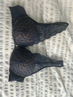 Mörkblå spets-bh med mönster intimissimi - Säljer en mörkblå bh med vackert spetsmaterial och detaljerat mönster. Bh:n har en liten rosett mellan kuporna och breda spetsband. Perfekt för dig som gillar stilrena och eleganta underkläder. Från intimissimi, tror att det är storlek 75B