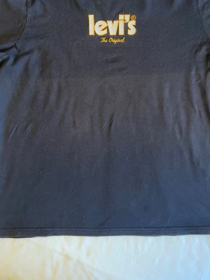 Svart Levi's t-shirt med logga - Snygg svart t-shirt från Levi's med gul logga och texten 'The Original' på bröstet. Klassisk passform och rund halsringning. Perfekt till jeans eller shorts för en enkel och stilren look.