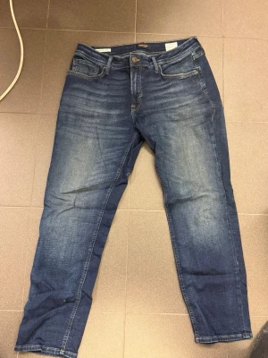 Mörkblå jeans från Jack&jones - Snygga mörkblå jeans från jack&jones med klassisk femficksdesign och diskreta slitningar framtill. Jeansen har raka ben och är tillverkade i mjuk bomullsdenim med lite stretch för extra komfort. Perfekta för en avslappnad och trendig look.