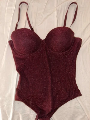 Glittrig vinröd body från intimissimi!!  - Säljer min jättefina body från intimissimi då den ej kommer till användning. Bara använd en gång! Köpt för cirka 700kr från intimissimi, säljer för 500kr 💕den är i storlek 75B/S