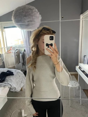Ljusgrå off shoulder stickad tröja - Trendig ljusgrå stickad tröja med off shoulder-design och långa ärmar. Tröjan har en smal passform och ribbstickad struktur som ger en snygg siluett. Perfekt för dig som vill ha en stilren men ändå unik look.