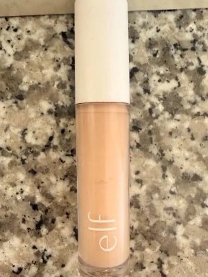 e.l.f. Hydrating Camo Concealer, Fair beige  - En flytande concealer från e.l.f. i nyansen fair beige. Produkten heter Hydrating Camo Concealer och kommer i en genomskinlig tub med vit kork. Perfekt för att täcka ojämnheter och ge en återfuktad finish. 