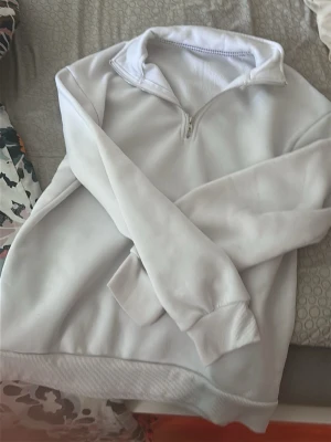 Vit halvzip hoodie - Snygg vit hoodie med halv dragkedja och hög krage. Tröjan har ribbade muddar vid ärmslut och nederkant, samt en avslappnad passform. Perfekt för en chill och stilren look. Materialet känns mjukt och bekvämt mot huden.