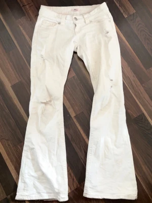 Vita bootcut jeans med slitningar - Säljer ett par lågmidjade vita jeans ifrån Gina 14+. Designen har hål framtil och diskret design på bakfickorna. Super fina men säljer då dem är lite för stora och har flera liknande. Priset kan diskuteras vid snabb affär.