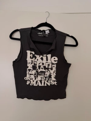 Svart croppad linnetopp H&M  - Svart croppad linnetopp från H&M med råa kanter och tryck 'Exile on Main St' framtill. Toppen är ärmlös och har en v-ringad hals. Perfekt för dig som gillar en edgy och avslappnad stil.