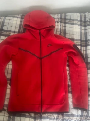 Röd Nike Tech Fleece hoodie - Säljer min röda nike tech hoodie i mycket bra skick, de enda slitaget är dragkedjan (syns på andra bilden) . Storlek xs skulle säga mer xs/s.