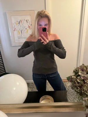 Mörkgrå off shoulder stickad tröja - Trendig mörkgrå stickad tröja med off shoulder-modell och långa ärmar. Tröjan har en ribbstickad struktur och sitter snyggt över axlarna. Perfekt för dig som vill ha en stilren och modern look. Använd endast 1 gång