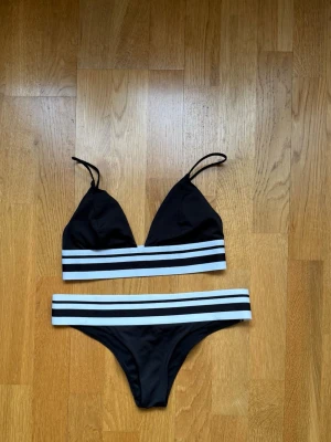 Svart bikini med vita ränder - Snygg svart bikini med breda vita och svarta ränder på både överdel och underdel. Överdelen har trekantskupor och smala axelband. Perfekt för stranden eller poolen!