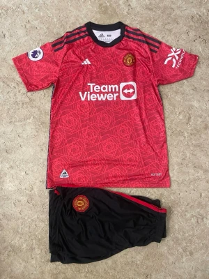 Manchester United matchställ Rashford - Säljer ett Manchester United matchställ från Adidas med Rashford 10 på ryggen. Tröjan är röd med svarta detaljer, klubbmärke och sponsortryck, samt Premier League-märke på ärmen. Shortsen är svarta med röd rand och klubbmärke. Perfekt för fotbollsträning eller match.