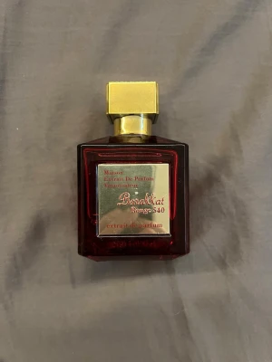 Baccarat Rouge 540 Extrait de Parfum - Lyxig parfymflaska i rött glas med guldigt lock från Maison Francis Kurkdjian. Baccarat Rouge 540 Extrait de Parfum har en fyrkantig form och en elegant metallisk etikett framtill. Perfekt för dig som gillar exklusiva dofter och snygg design.