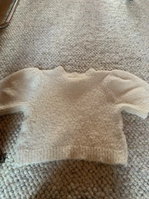Vit fluffig stickad tröja - Supersöt vit stickad tröja med puffärmar och rund hals. Tröjan är gjord i ett mjukt, fluffigt material som känns riktigt mysigt. Perfekt för dig som gillar en enkel men trendig look med volym i ärmarna.