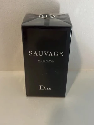 Dior Sauvage Eau de Parfum - Dior Sauvage Eau de Parfum i en elegant svart rektangulär kartong med vit text. Förpackningen har en lyxig känsla och pryds av Diors logotyp på toppen. Parfymen är känd för sin fräscha och maskulina doftprofil.