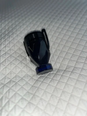 Paco Rabanne Invictus Victory parfym - Säljer en Paco Rabanne Invictus Victory parfym i en cool mörkblå troféformad flaska med svarta detaljer och ett stort V i guld på framsidan. Flaskan är tillverkad i glas och plast och har en modern, sportig design.